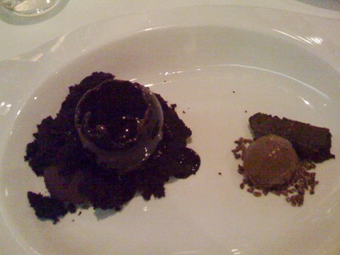 made of win. and chocolate. a partially melted hollow chocolate sphere with a dollop of fudge within, surrounded by rich chocolate cake on the left; on the right, a dollop of black olive ice cream surrounded by minced cacao nibs, and a small, thin brownie slice